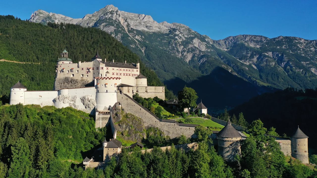 Hohenwerfen Castle surrounded by forest with dramatic Austrian Alps rising behind its fortified walls.