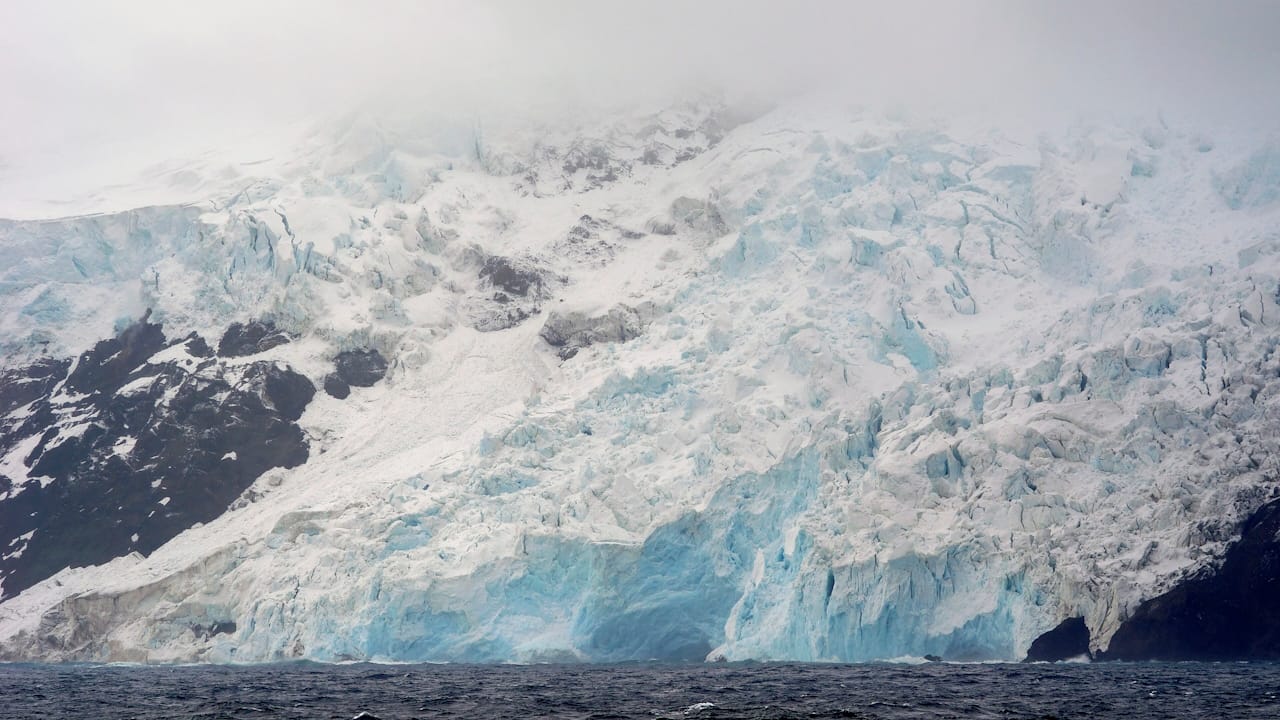 Massive blue-white glacier descends into dark ocean waters on isolated Bouvet Island.