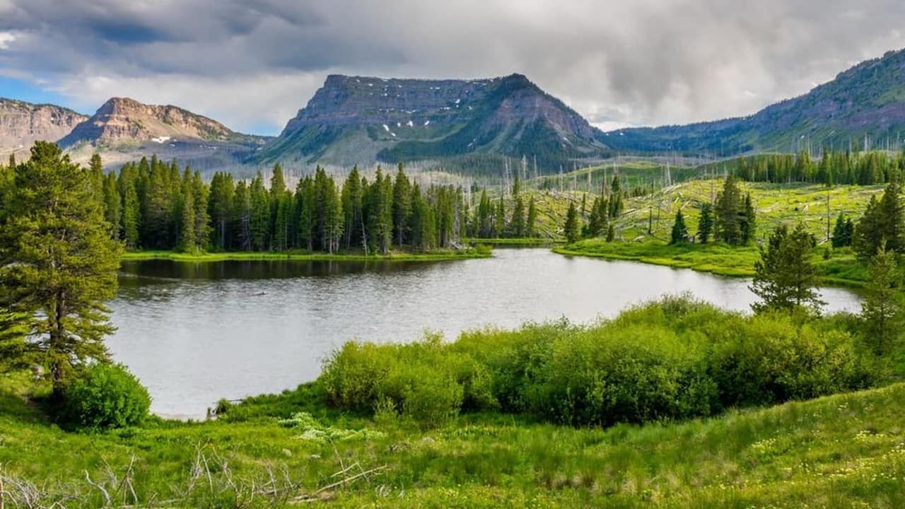 A picturesque lake bordered by trees and mountains, showcasing Amphitheater Peak in the Flat Tops Wilderness area.