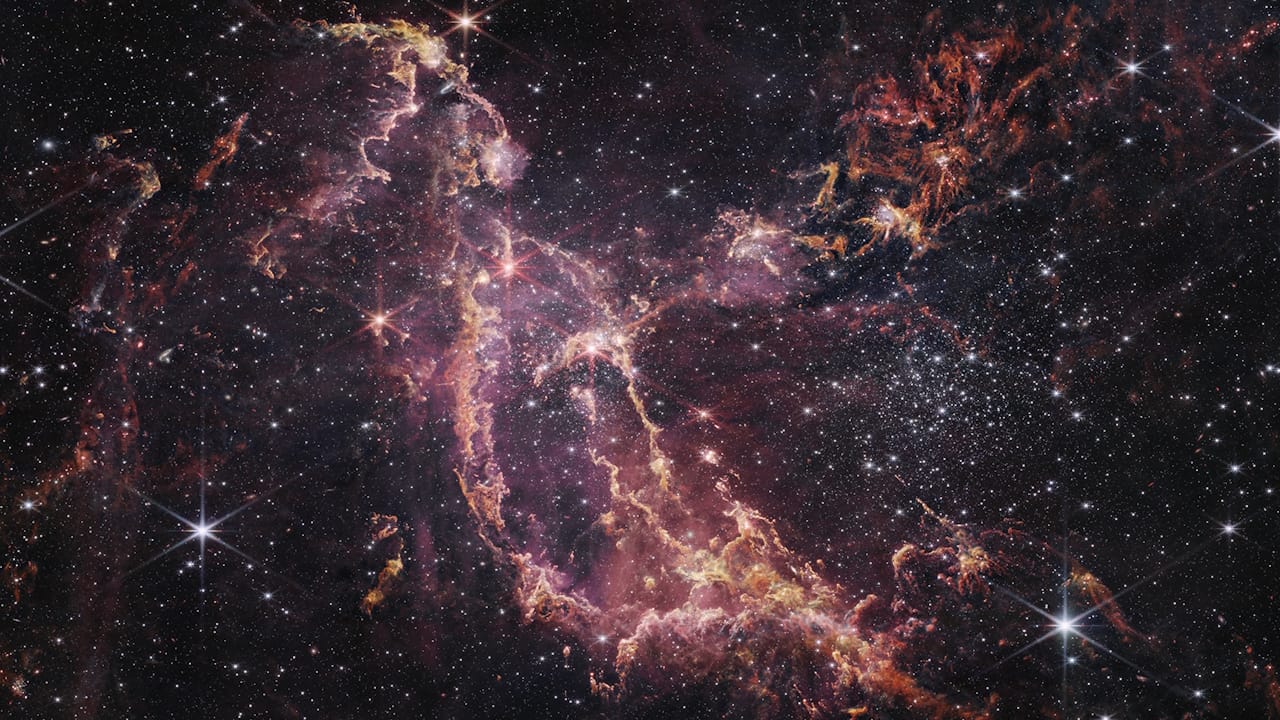 Stunning infrared view of NGC 346 nebula, showcasing vibrant pink and orange hues from young stars and cosmic dust.