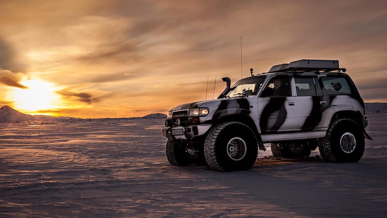 Older Land Cruiser 80 Series on 44 inch tires with desert white camouflage paint driving on a snowy surface.