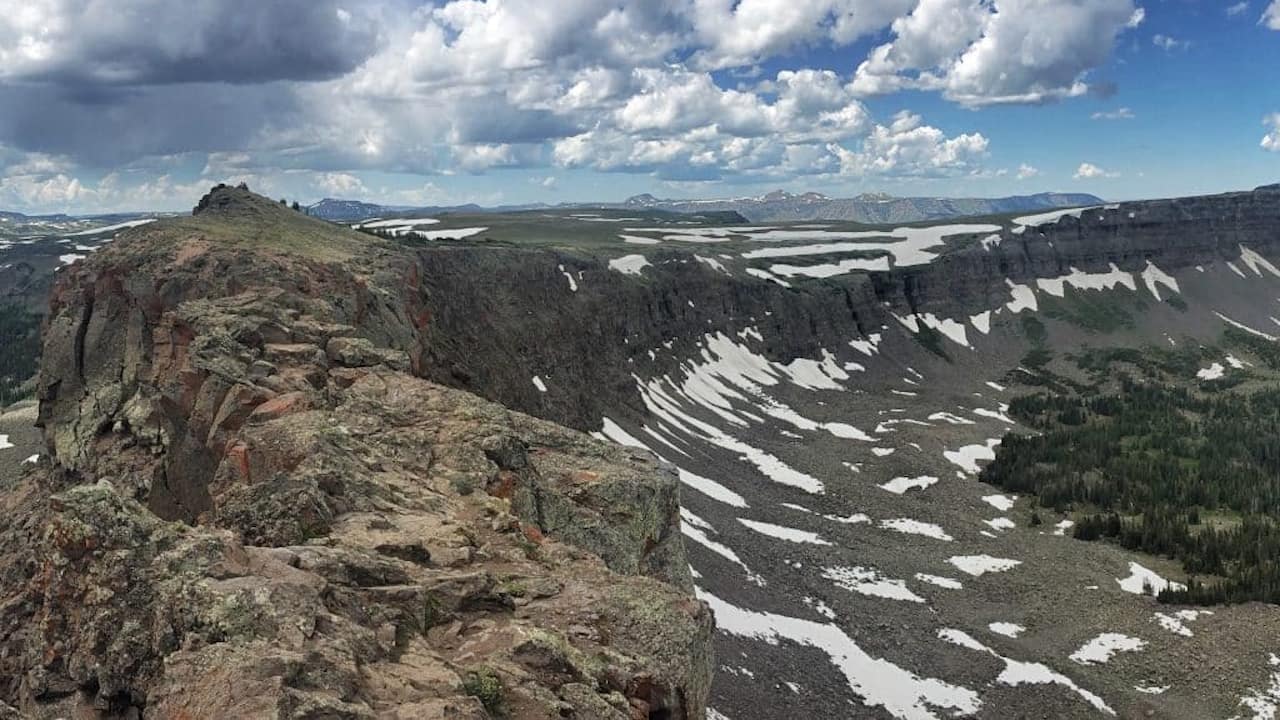 Overlooking the rugged Devil's Causeway ridgeline in the Flat Tops Wilderness area with mountains in the distance and a partly cloudy sky.