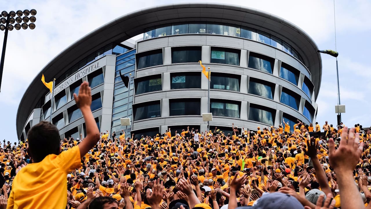 Fans in yellow shirts and black hats unite in a heartfelt wave, honoring the Hawkeye Wave tradition for children in the hospital.