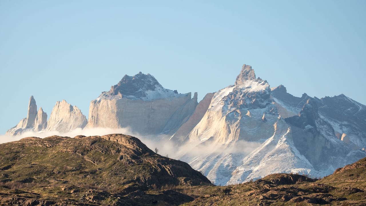 Snow-covered peaks of the stunning Torres del Paine mountain range rise majestically against a clear blue sky.