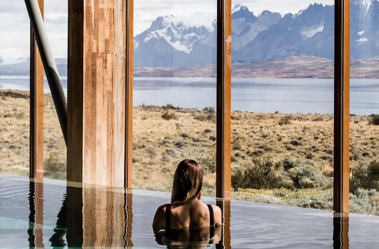 A serene scene of a woman in a pool at Tierra Patagonia hotel, framed by the breathtaking Torres del Paine mountains.
