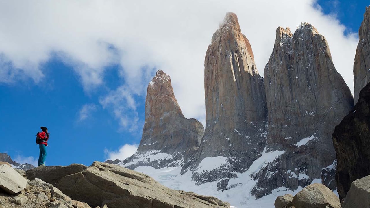 A woman stands on a rock, gazing at the iconic granite spires of Torres del Paine, embracing nature's grandeur.