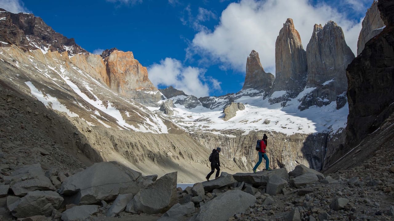 Two hikers traverse rocky terrain in Torres del Paine National Park on Three Towers hiking trail, surrounded by majestic mountain peaks.