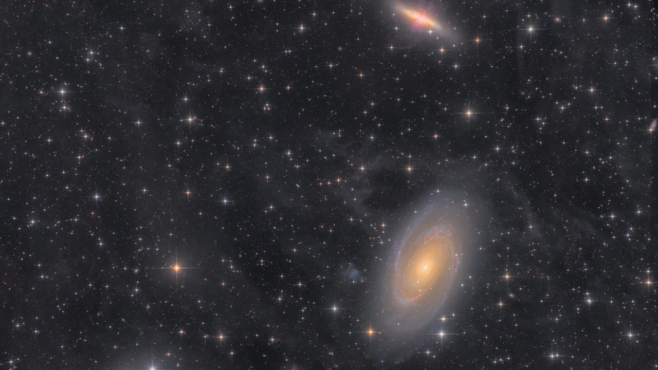 View of M81 and M82 galaxies, showcasing spiral arms and star-forming regions against a backdrop of interstellar clouds.