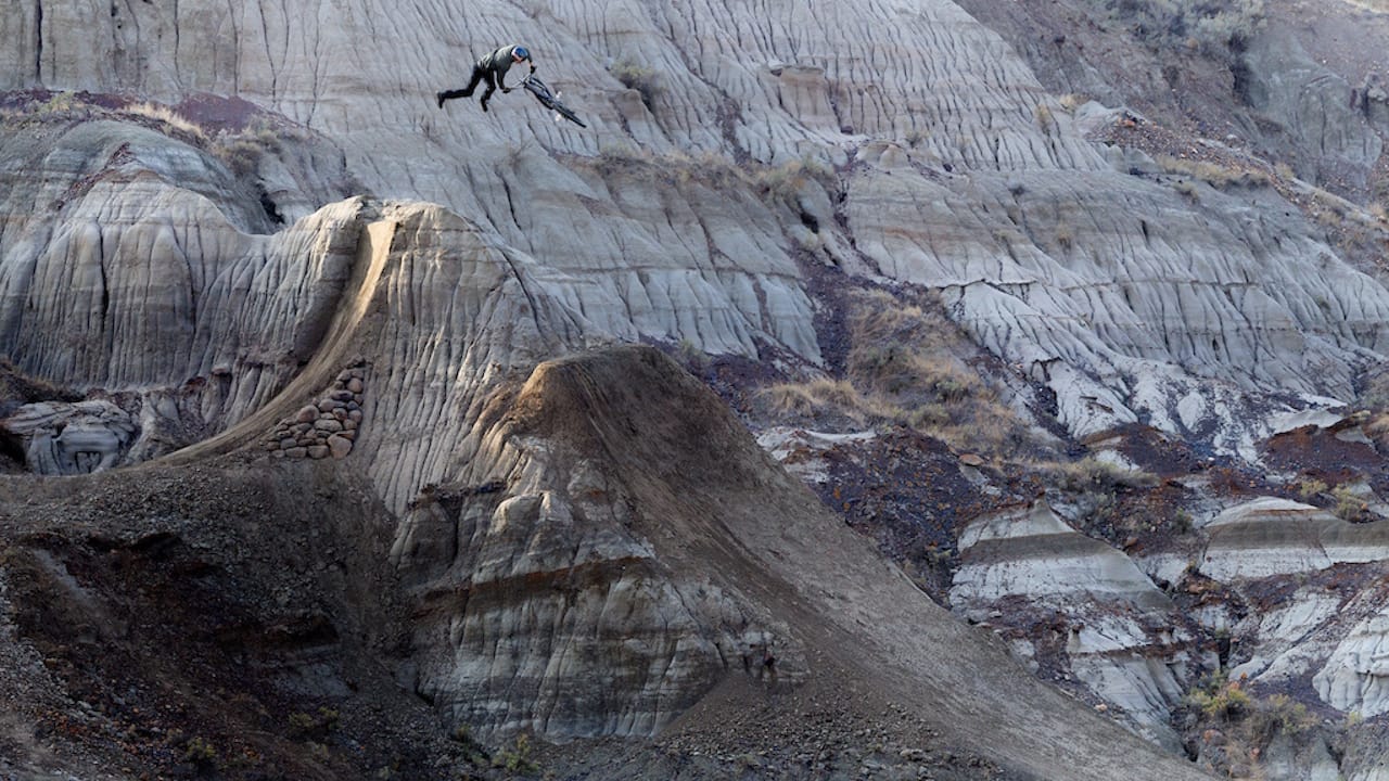 A mountain biker shown jumping his bike with a background of the Canadian Badlands.