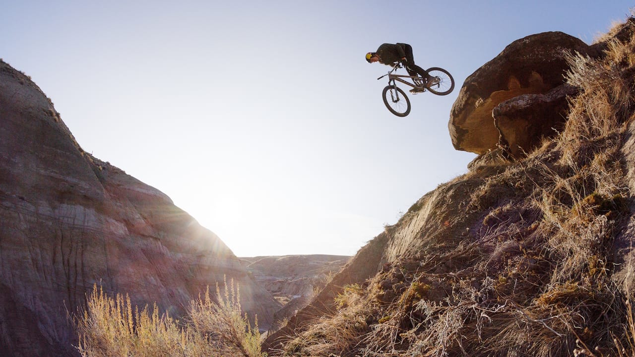 A mountain biker jumping his bike off of a big rock.