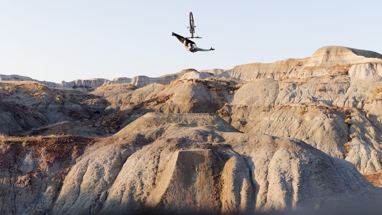 A mountain biker flying through the air doing a freestyle trick holding on with one hand.