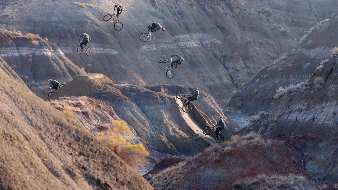 A timelapse image showing Brandon Semenuk jumping his mountain bike on a ramp made on a large dirt hill.