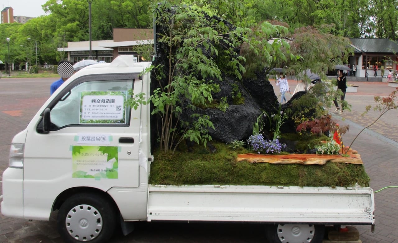 Garden in the back of a small truck with small trees and a large rock.