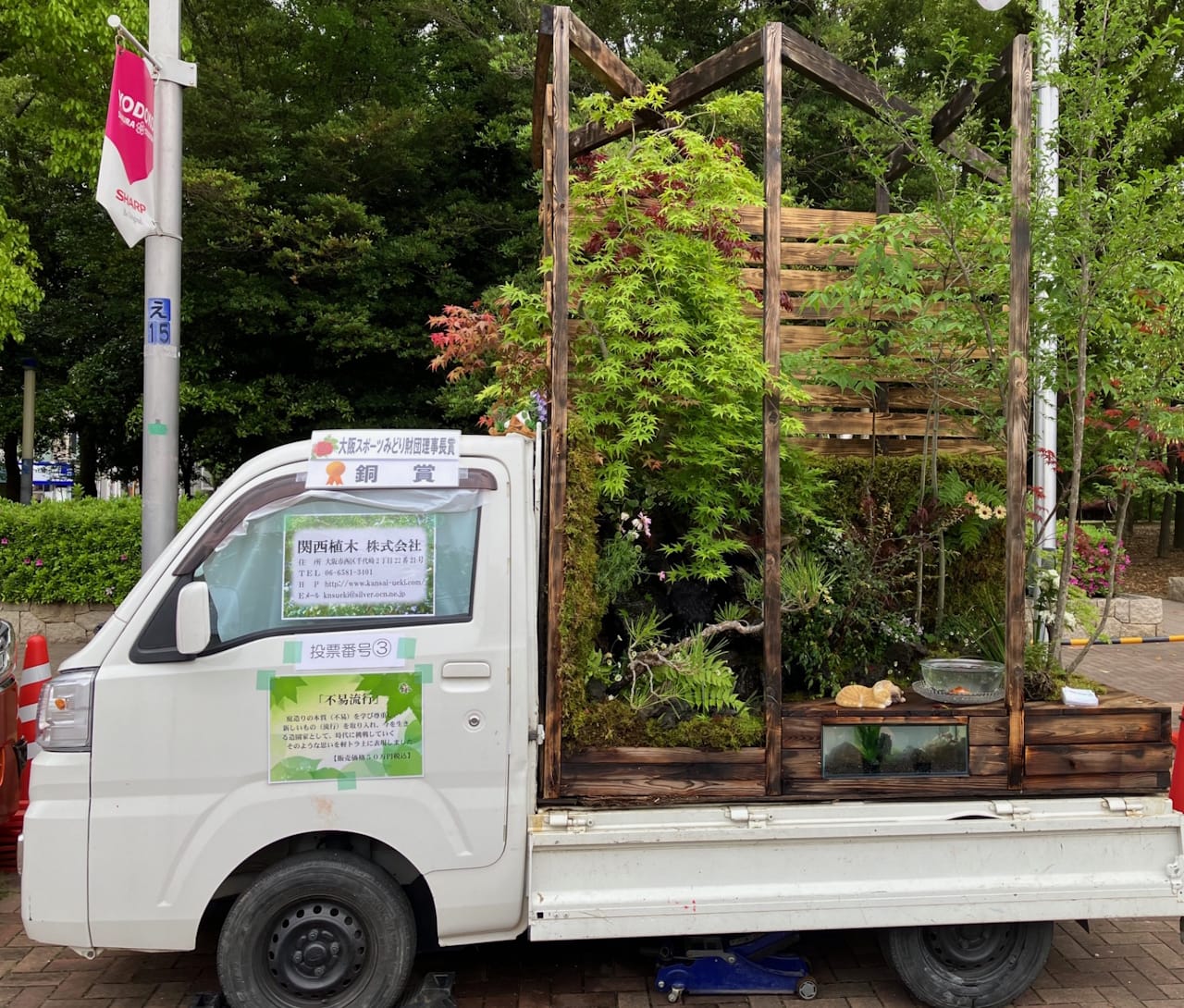 A tall structure with one wall enclosing a garden rising out of the bed of a Kei Truck.