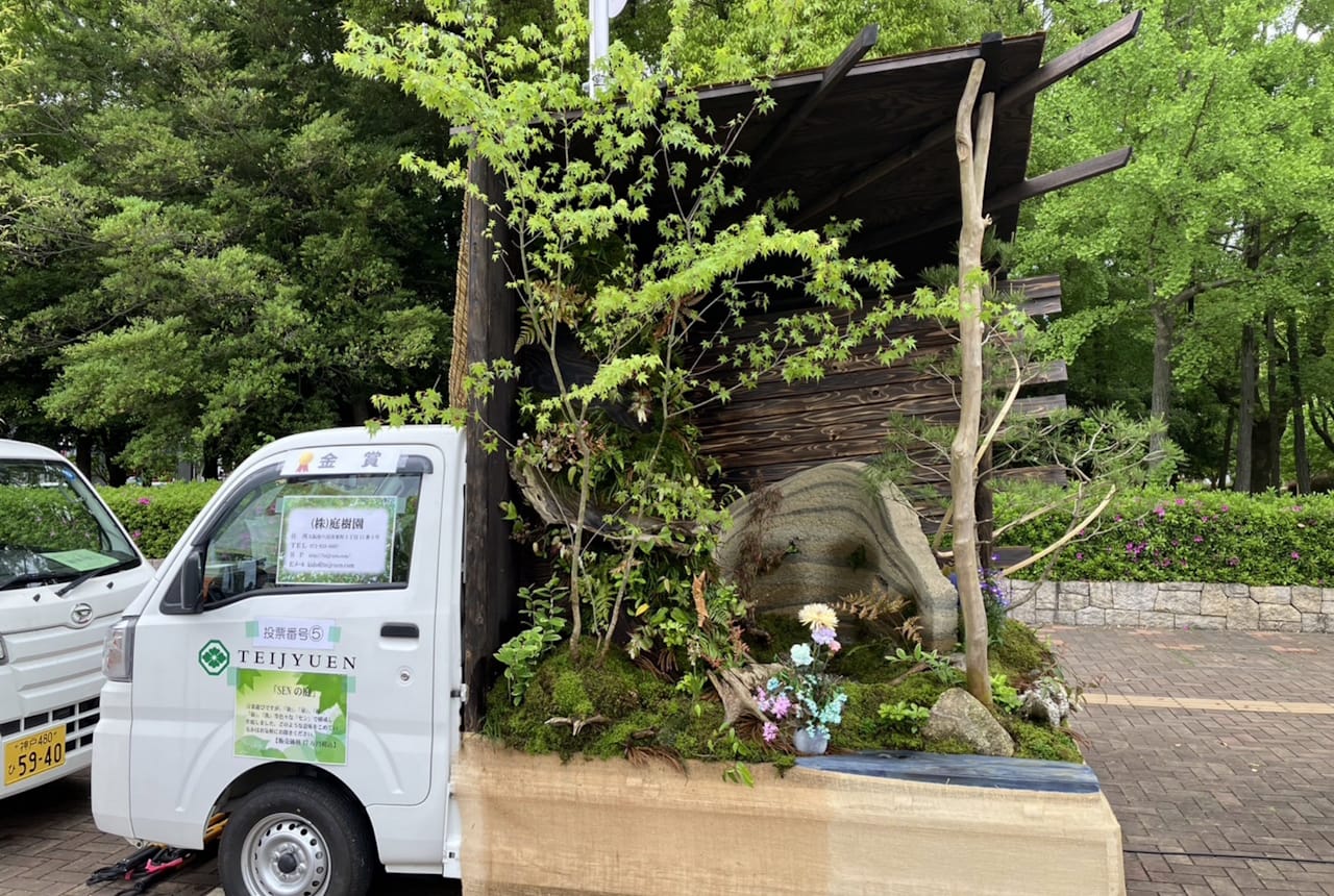 A tall structure with two walls enclosing a garden rising out of the bed of a small truck.