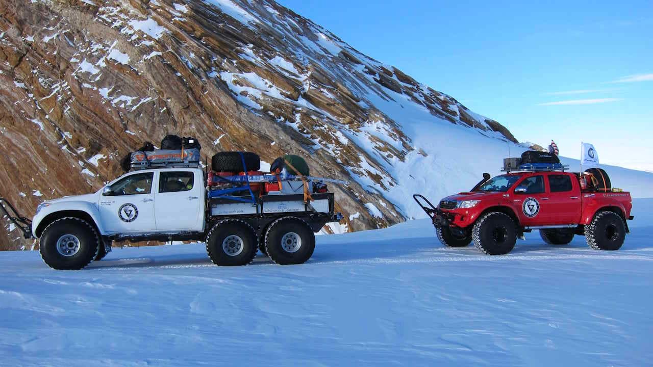 White 6x6 Toyota and red 4x4 heavily modified trucks participate in in a 2013 Antarctic expedition.