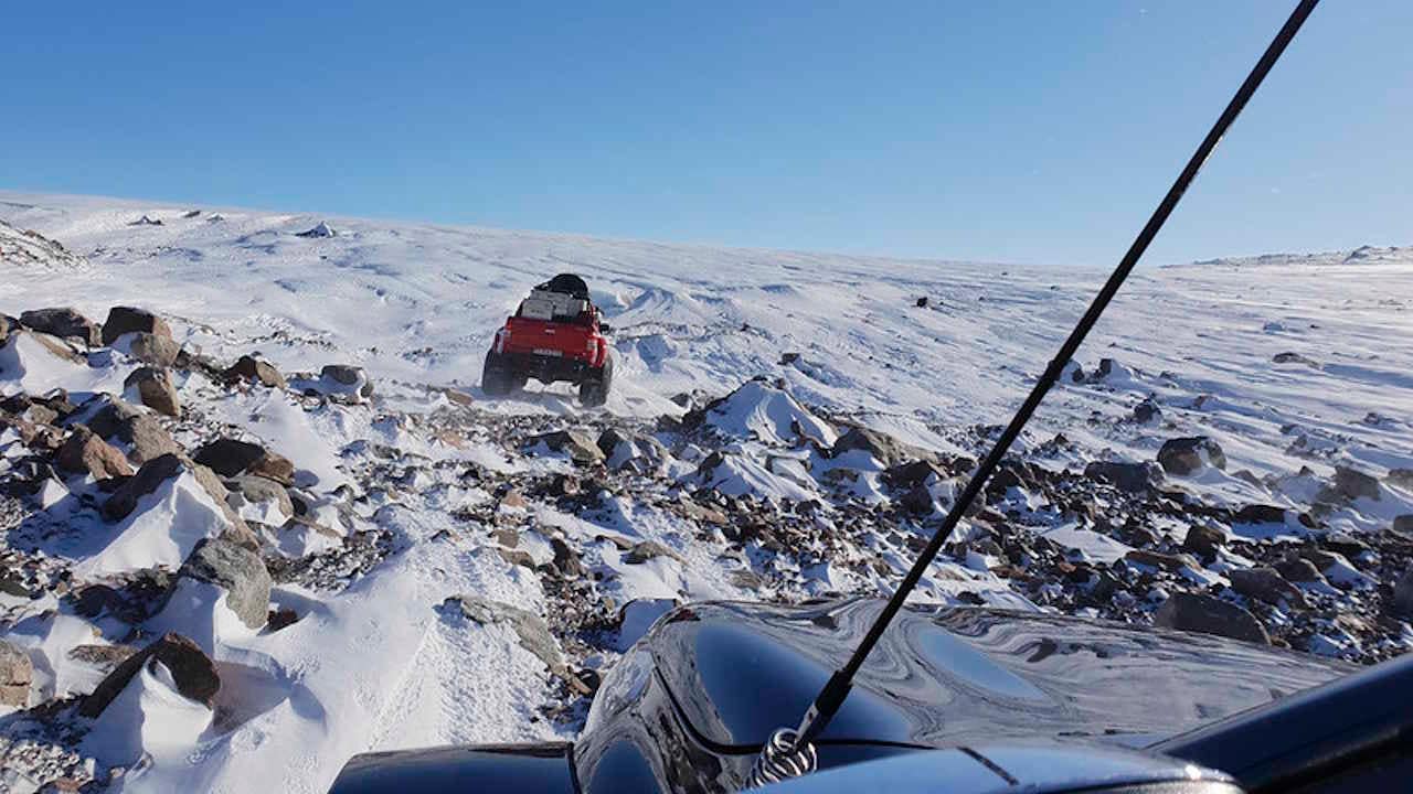 A red Arctic Trucks expedition vehicle shown in the distance in a picture taken from a blue expedition truck following it.