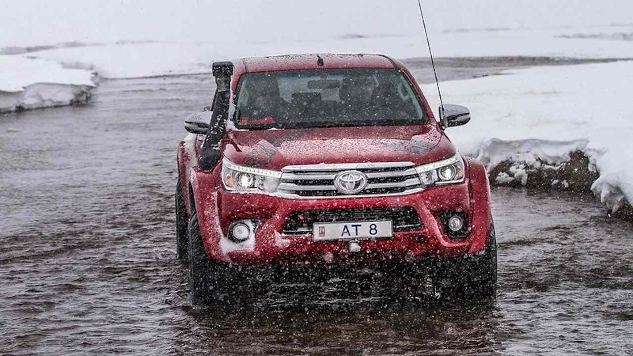 Red Toyota Hilux AT8 shown driving in a river in a snowy winter scene.