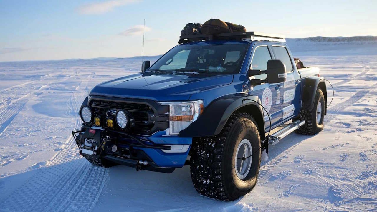 Highly modified blue Ford F150 cold weather expedition truck parked on flat snowy tundra.