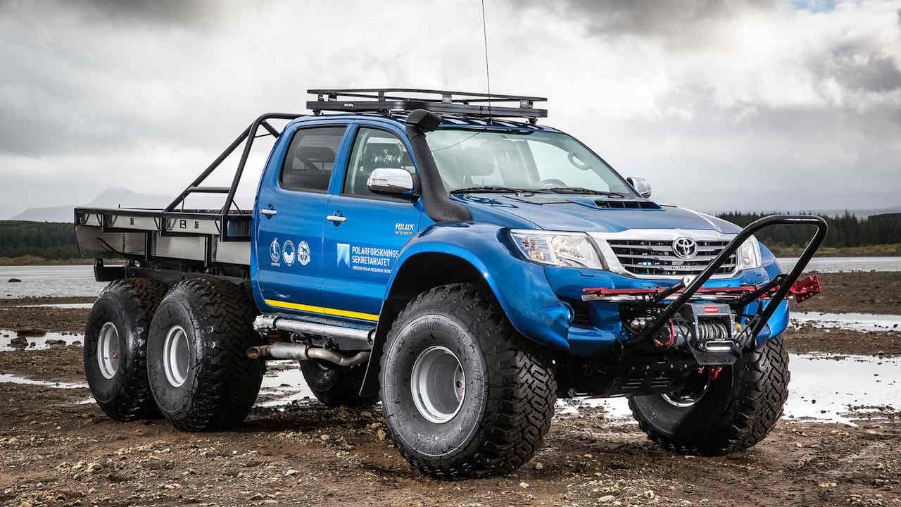 Blue 6x6 Toyota Hilux work truck with flat bed parked on a mud flat. 