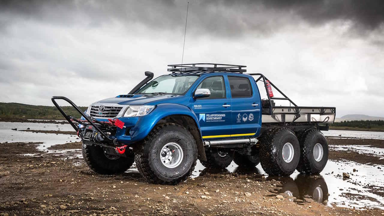 Blue Toyota Hilux 6x6 with flat bed shown in mud and water.