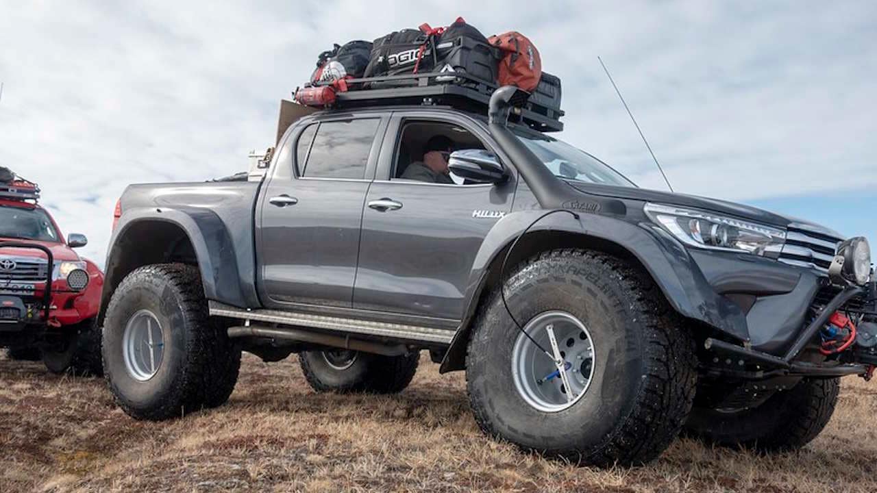 Grey Artic Trucks Toyota AT 44 shown crossing a small hill in dry tundra.