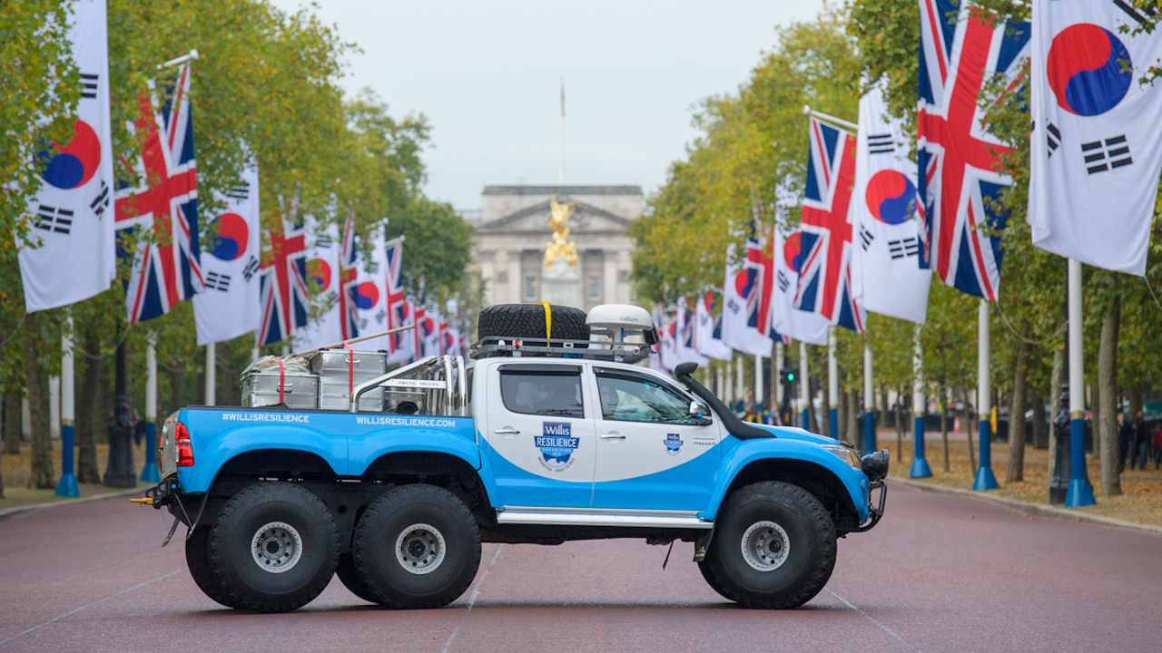 6x6 Toyota Hilux blue and white truck in London with English and Korean flags on both sides of the street.