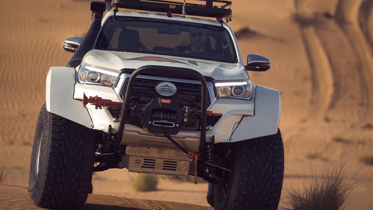 White Arctic Trucks Toyota Hilux with 44 inch studded tires in the sandy desert.
