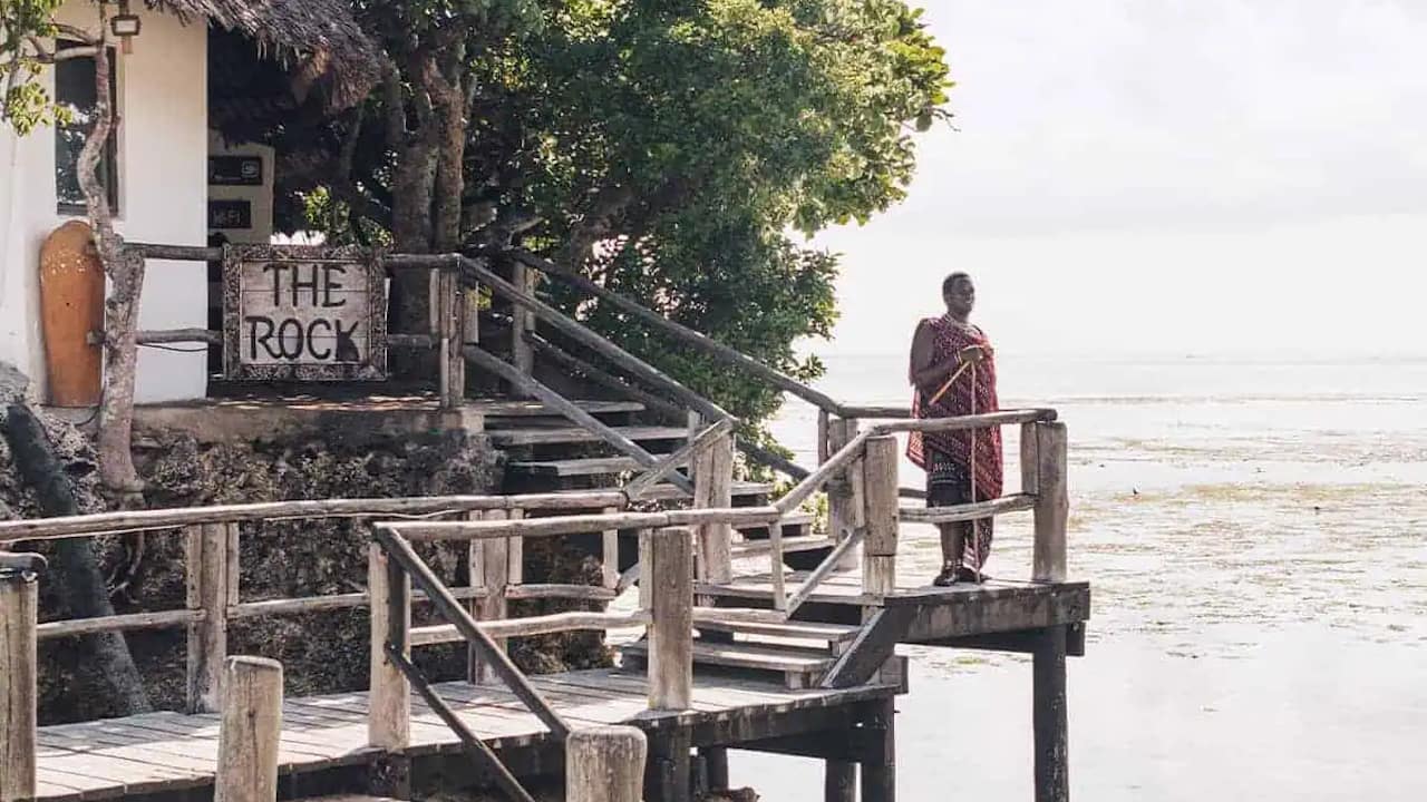 Zanzibari local in traditional dress standing on the front porch of a restaurant.