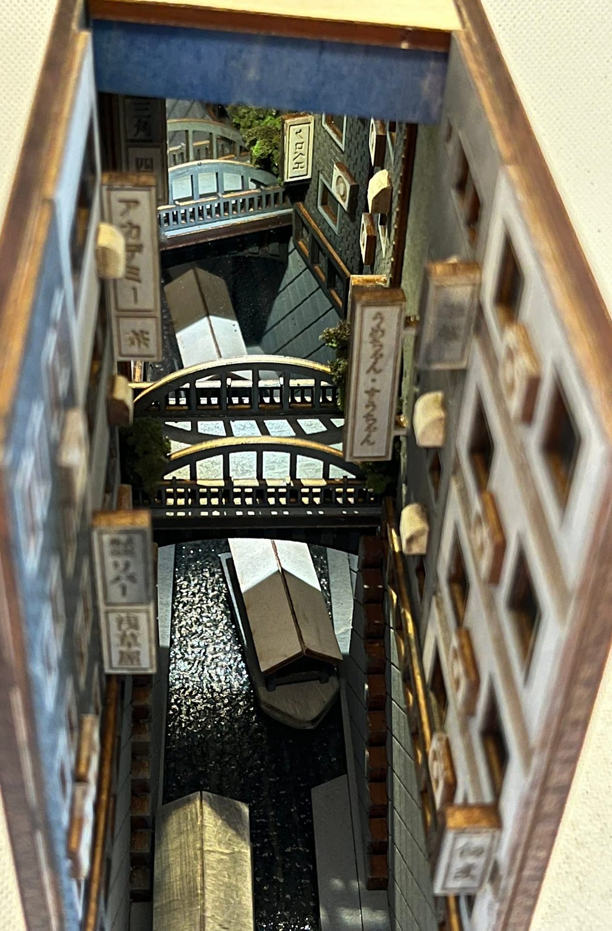 Picture of a book nook by Monde showing a narrow canal scene with small barges in the water and bridges above.