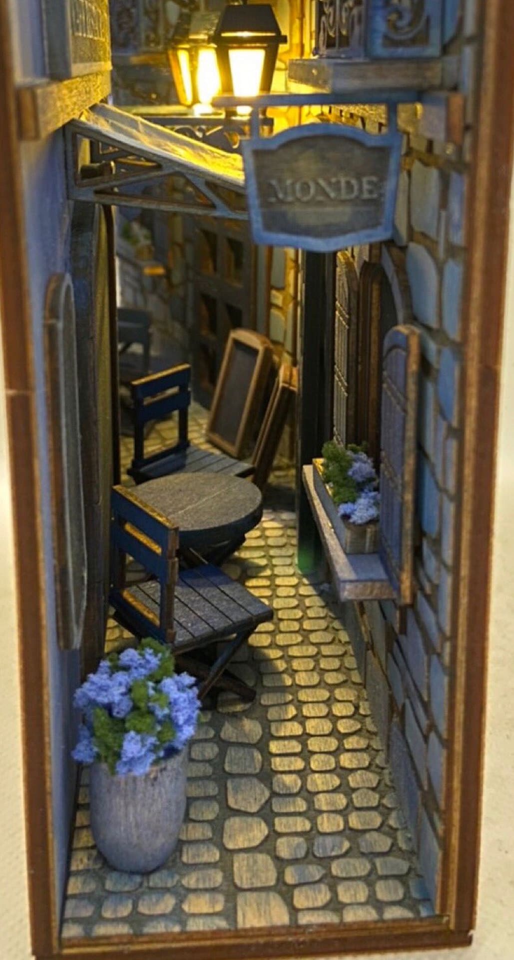 Book nook scene showing a narrow alley restaurant with blue cobblestones and blue tile on the walls and blue flowers.